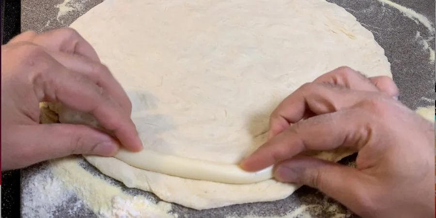 Hands folding and sealing pizza dough edges with mozzarella cheese filling using a fork technique.