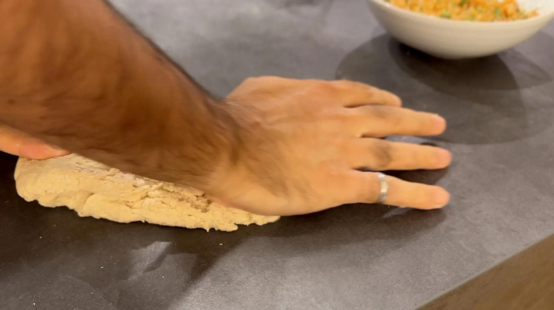 Hand kneading smooth paratha dough on a dark surface with bowls of ingredients nearby.