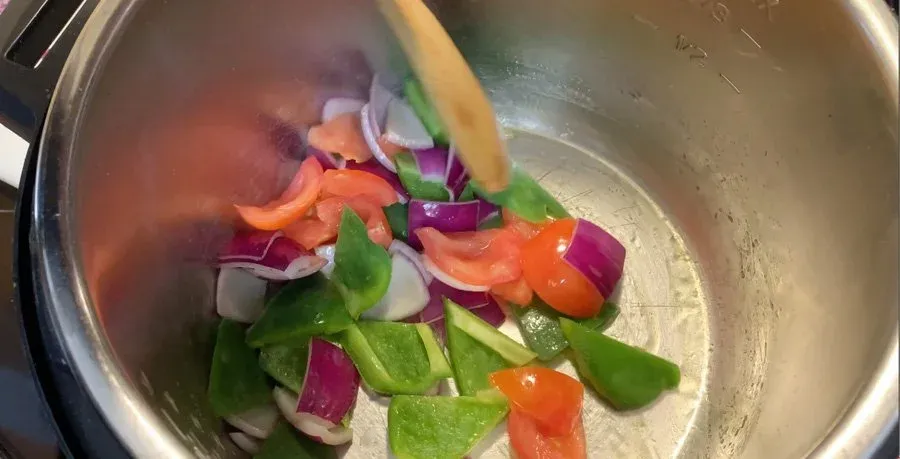 Diced red onion, green bell pepper, and orange bell pepper being sautéed in an Instant Pot on high heat.