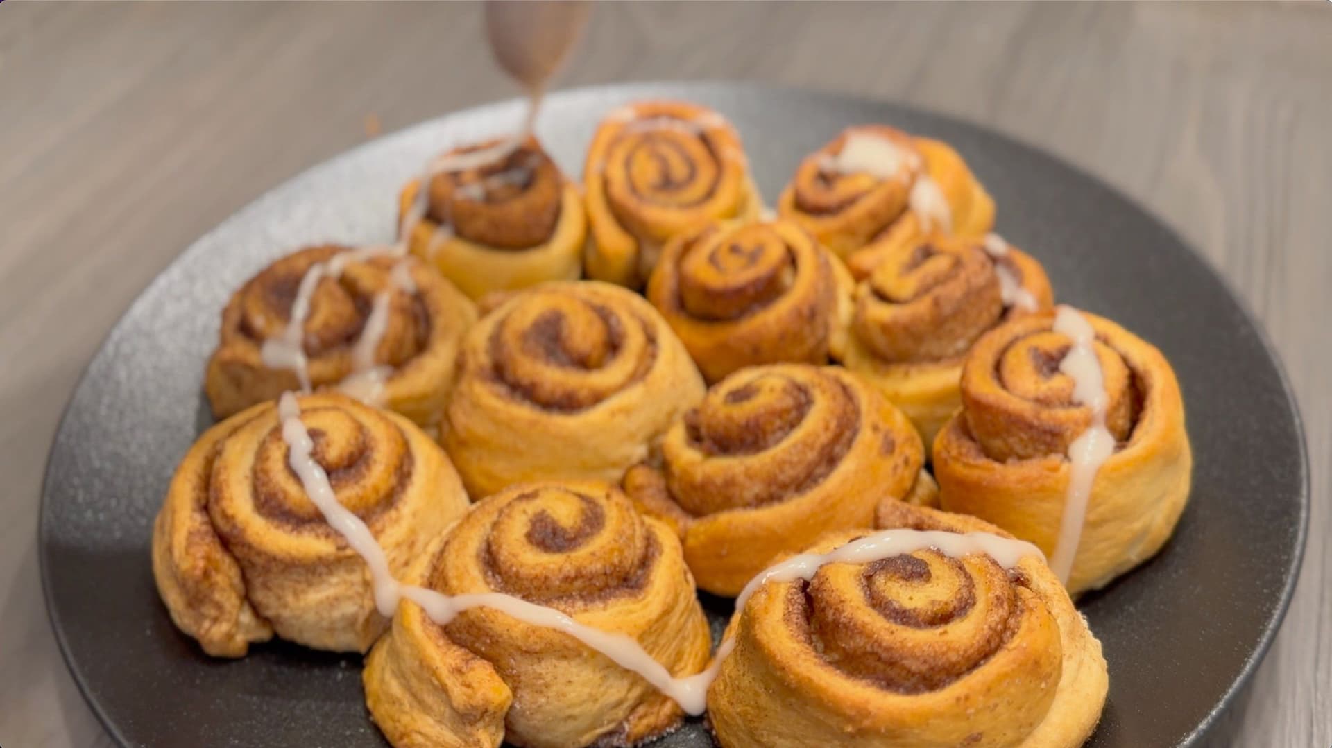 Freshly baked crescent roll cinnamon rolls with white icing drizzle on a gray plate.