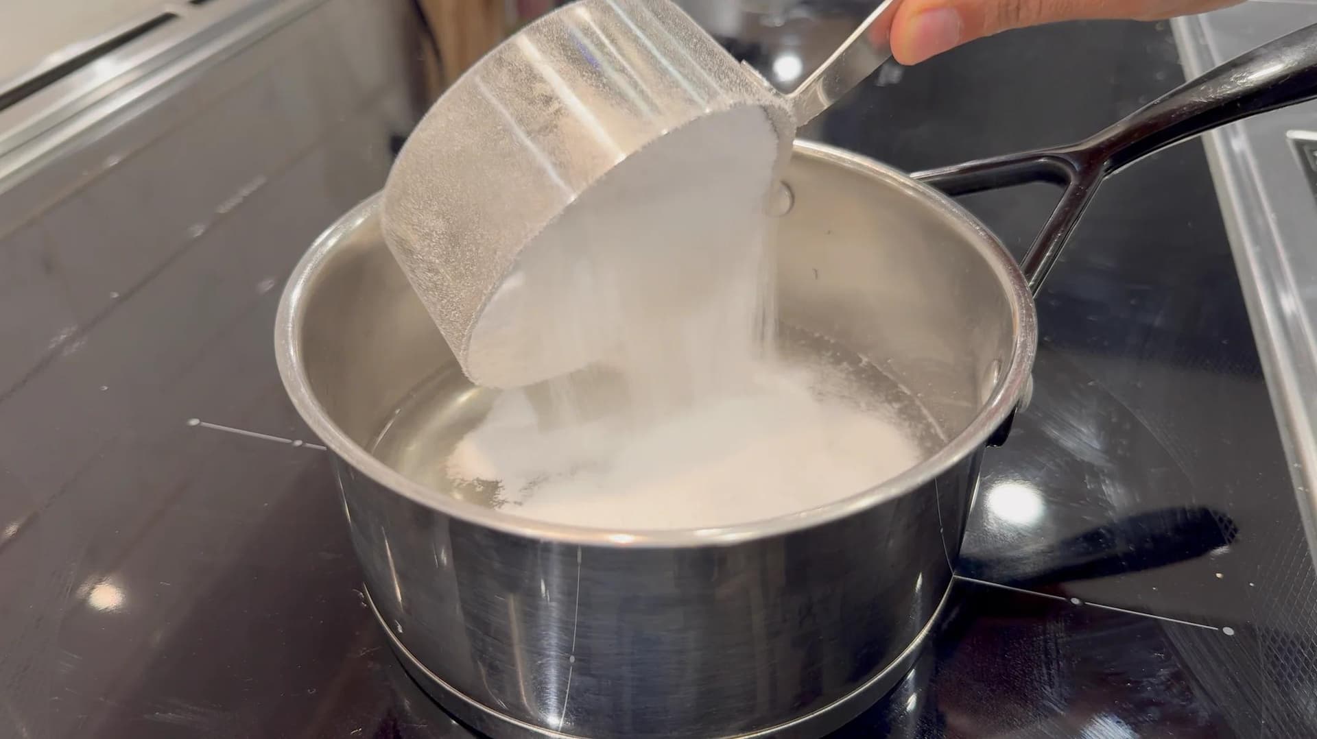 Sugar being poured into a saucepan of water on the stovetop while making vanilla syrup.