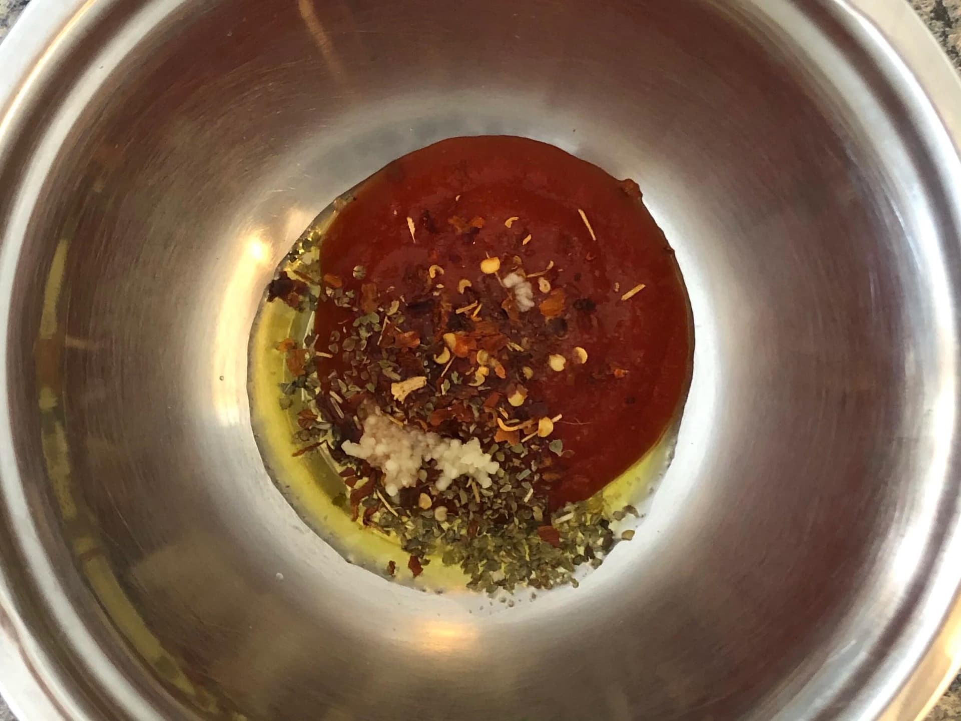 Passata with oregano, garlic, olive oil, and chili flakes mixed in a stainless steel bowl.