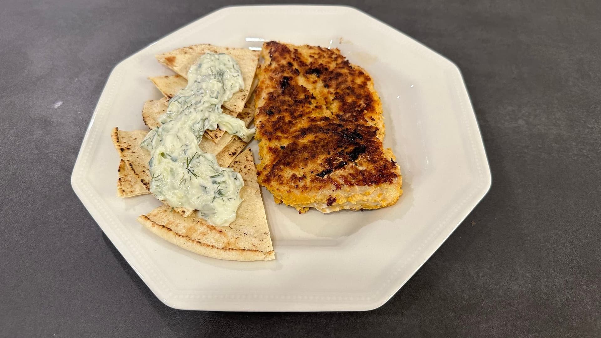 Homemade tzatziki sauce served with toasted pita bread on a white plate.