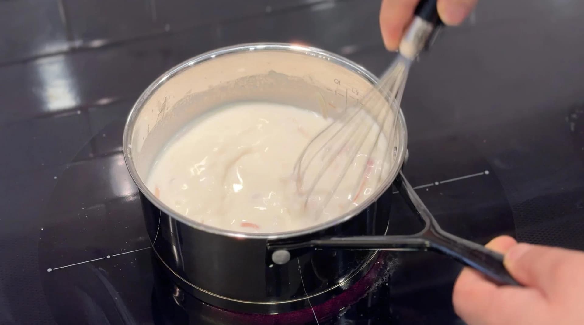 Whisking creamy béchamel sauce in a saucepan on the stovetop during preparation.