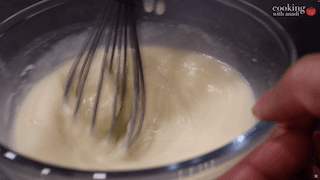 Whisking wet ingredients (milk, sugar, egg, melted butter) together in a bowl with a whisk.