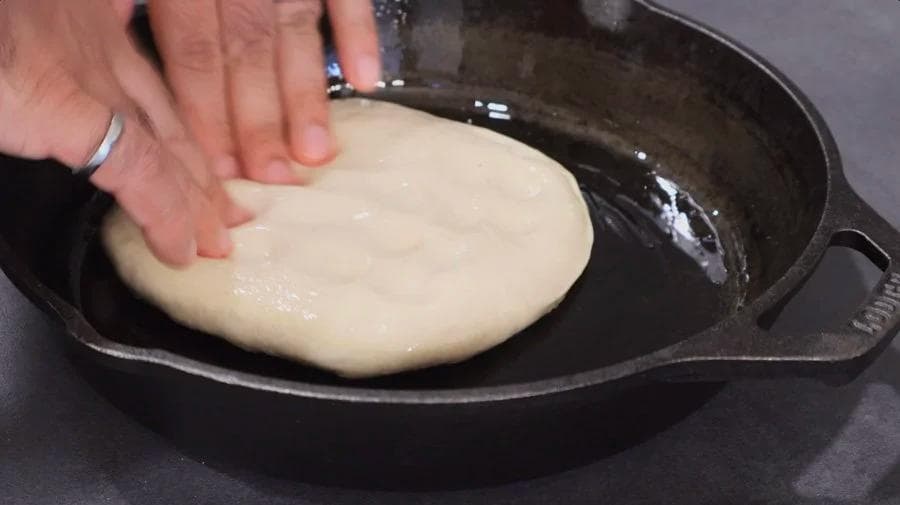 Hand stretching pizza dough in oiled cast iron skillet