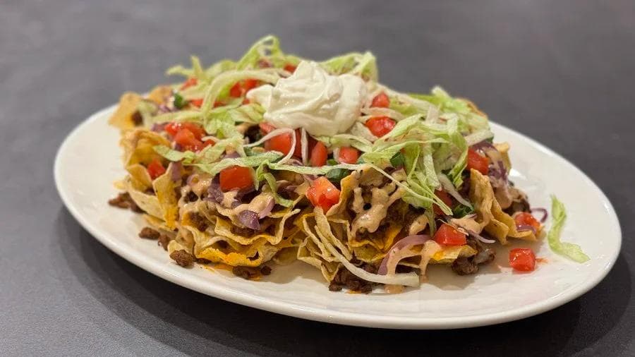Crazy Cheeseburger Nachos topped with seasoned ground beef, melted cheese, shredded lettuce, diced tomatoes, and jalapeños on a white plate.