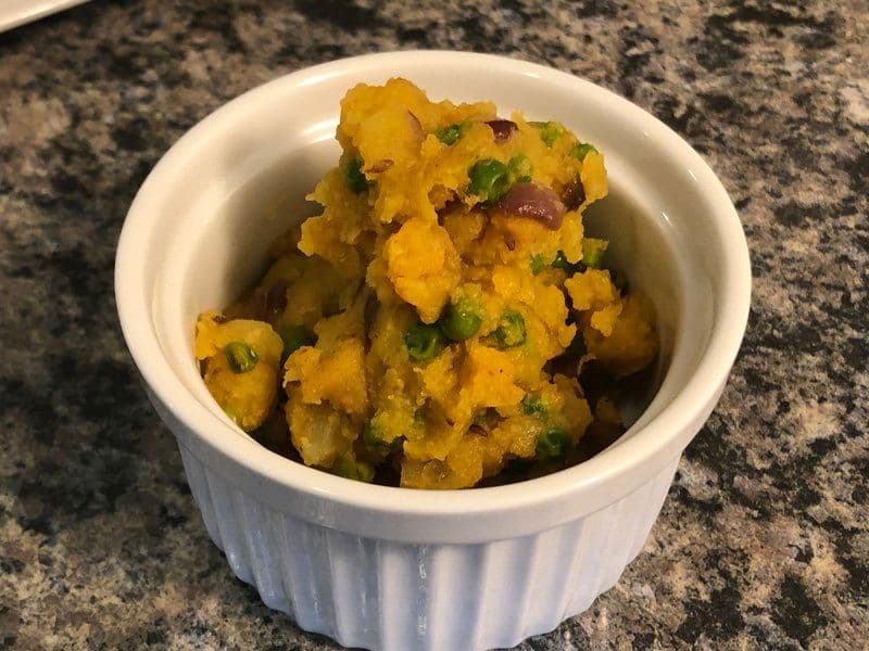 Spiced potato curry with green chilies in a white bowl on a granite countertop.