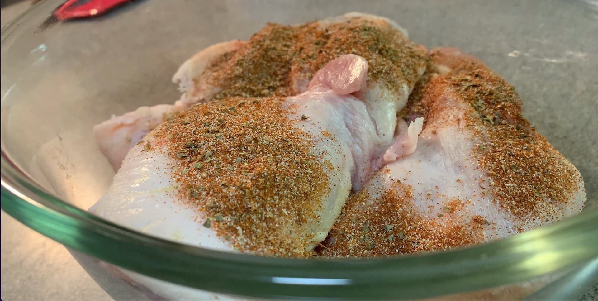 Raw chicken pieces coated in seasoned flour mixture in a glass bowl, ready for frying.