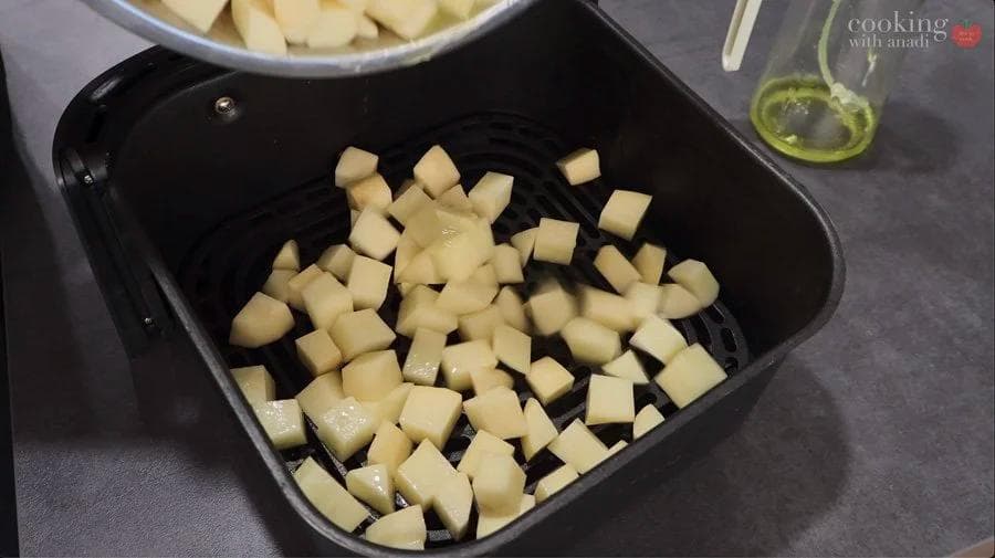 Cubed potatoes coated in oil arranged in a black air fryer basket before cooking.