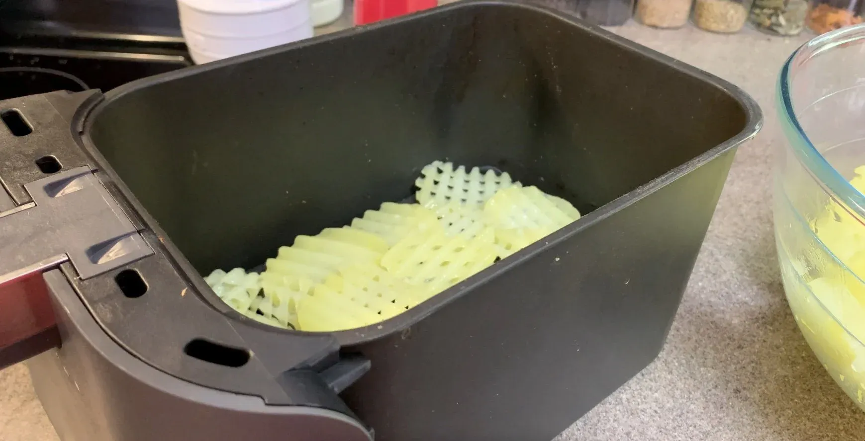 Waffle-cut potato fries arranged in a single layer in an air fryer basket before cooking.