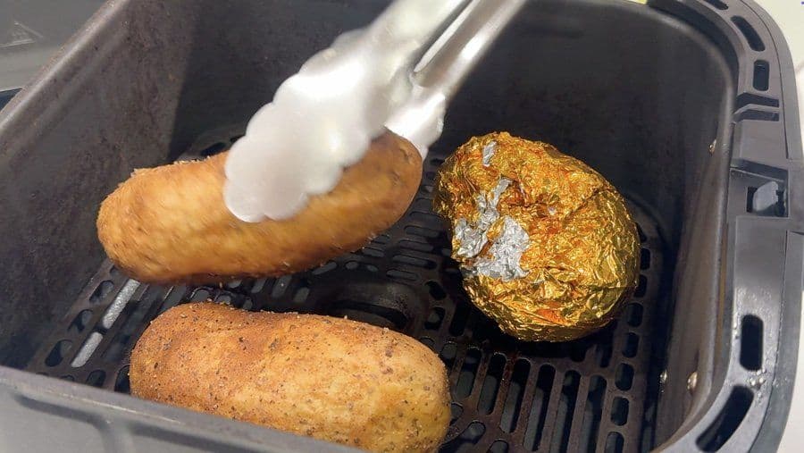 Cooked potatoes in air fryer basket, one being pricked with fork, golden crispy skins visible