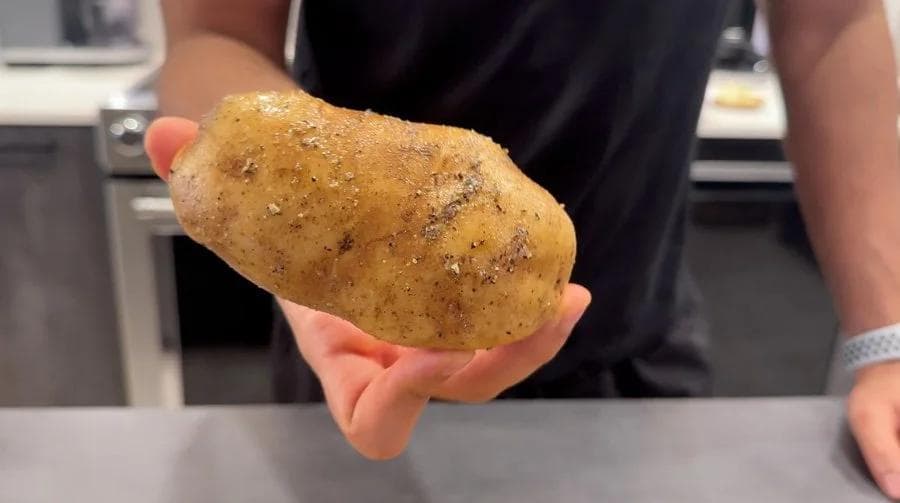 Hand holding a seasoned potato rubbed with olive oil, salt, and pepper, ready for air frying.