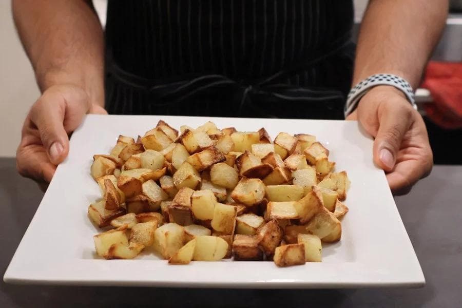 Crispy golden air fryer roasted potatoes served on a white square plate, held by hands.