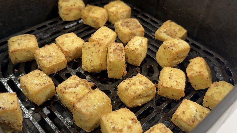 Golden-brown tofu cubes mid-cooking in an air fryer basket, showing crispy exterior.