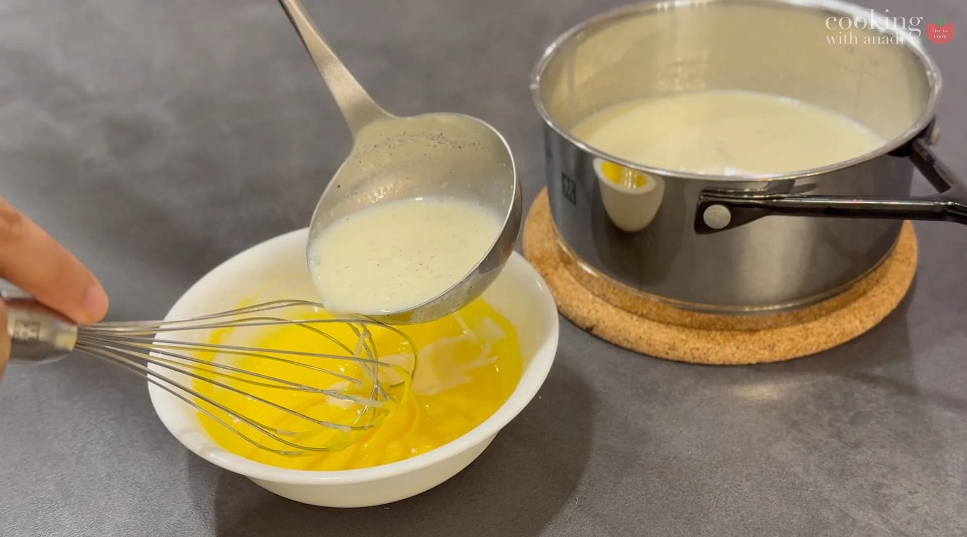 Tempering egg yolks by slowly pouring hot milk into cornstarch and yolk mixture while whisking.