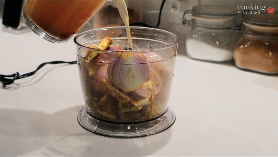 Liquid spice paste being poured into a food processor containing onions and other ingredients for rendang curry.