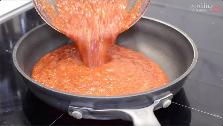 Red salsa being poured from a blender into a simmering pan on the stovetop.