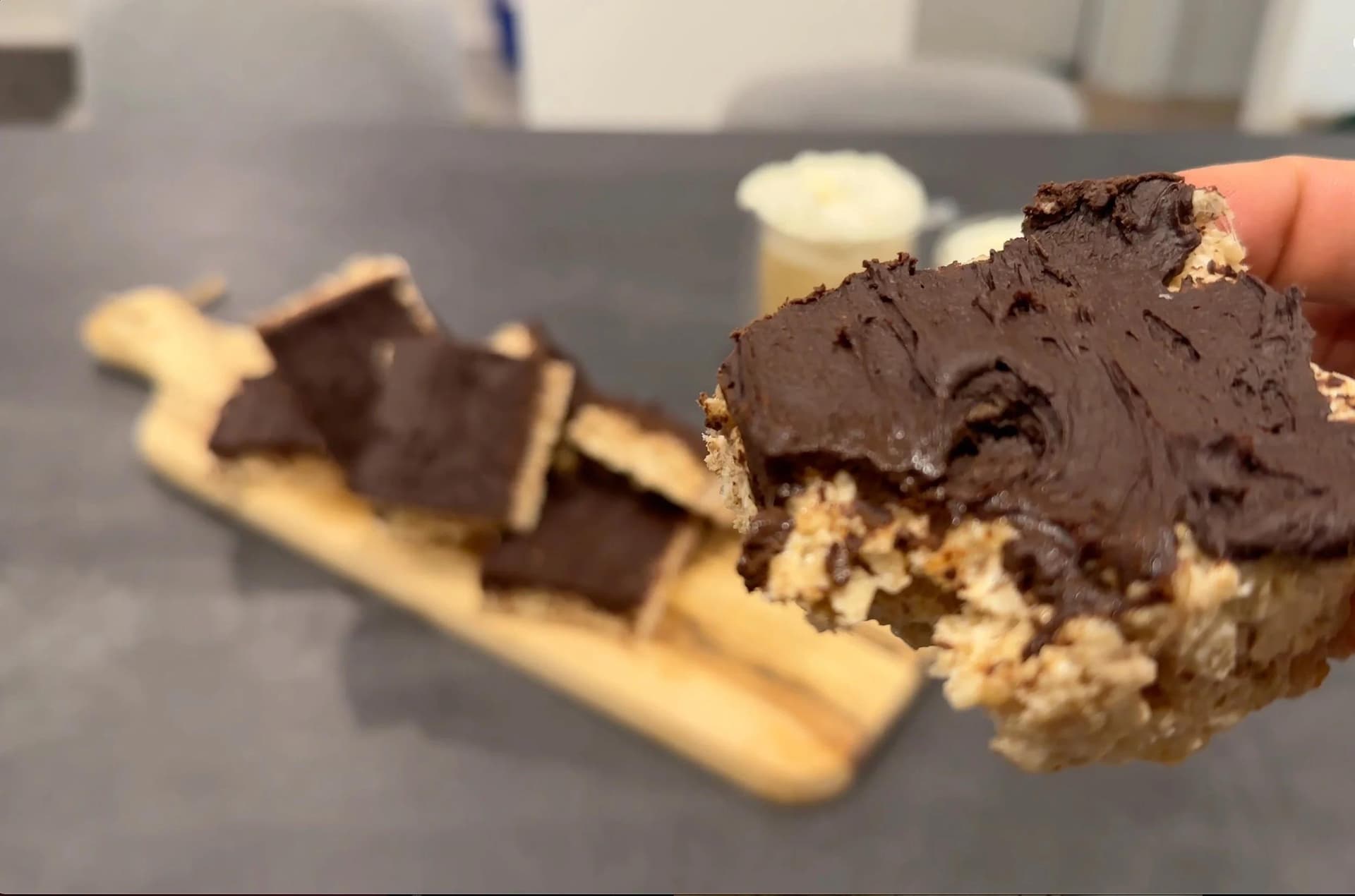 Sliced protein Rice Krispies treat with dark chocolate topping and crispy rice cereal base, held in hand.