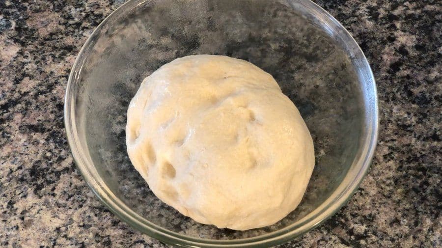 Smooth, pale tandoori naan dough resting in a greased glass bowl after the first 2-hour rise.