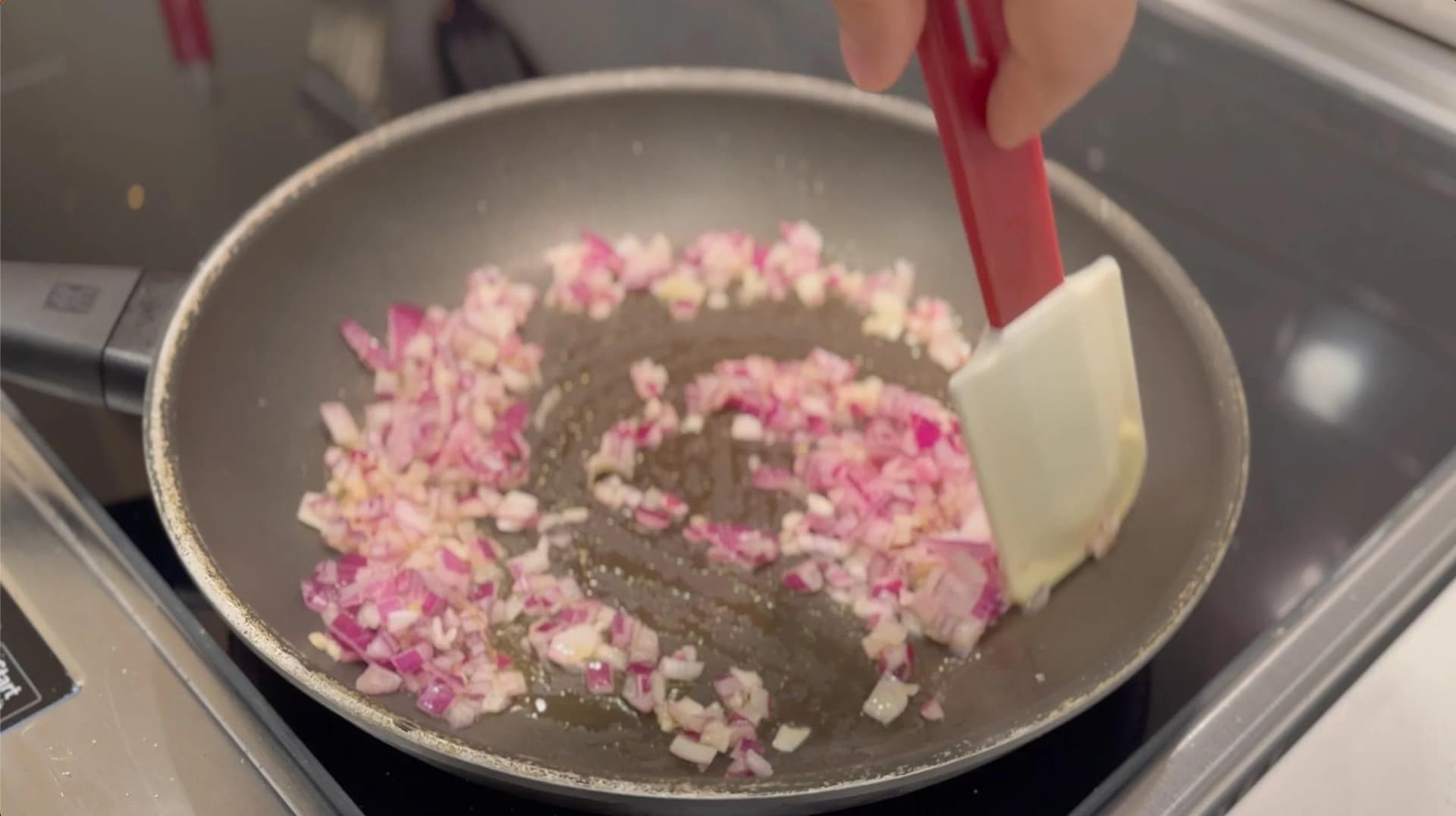 Diced pink and white onions being sautéed in oil in a gray pan with a spatula, for Mexican tomato rice.