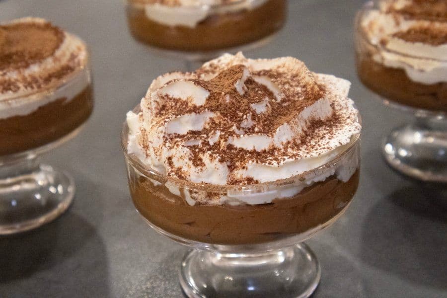 Rich chocolate mousse topped with whipped cream and cocoa powder in individual glass cups.