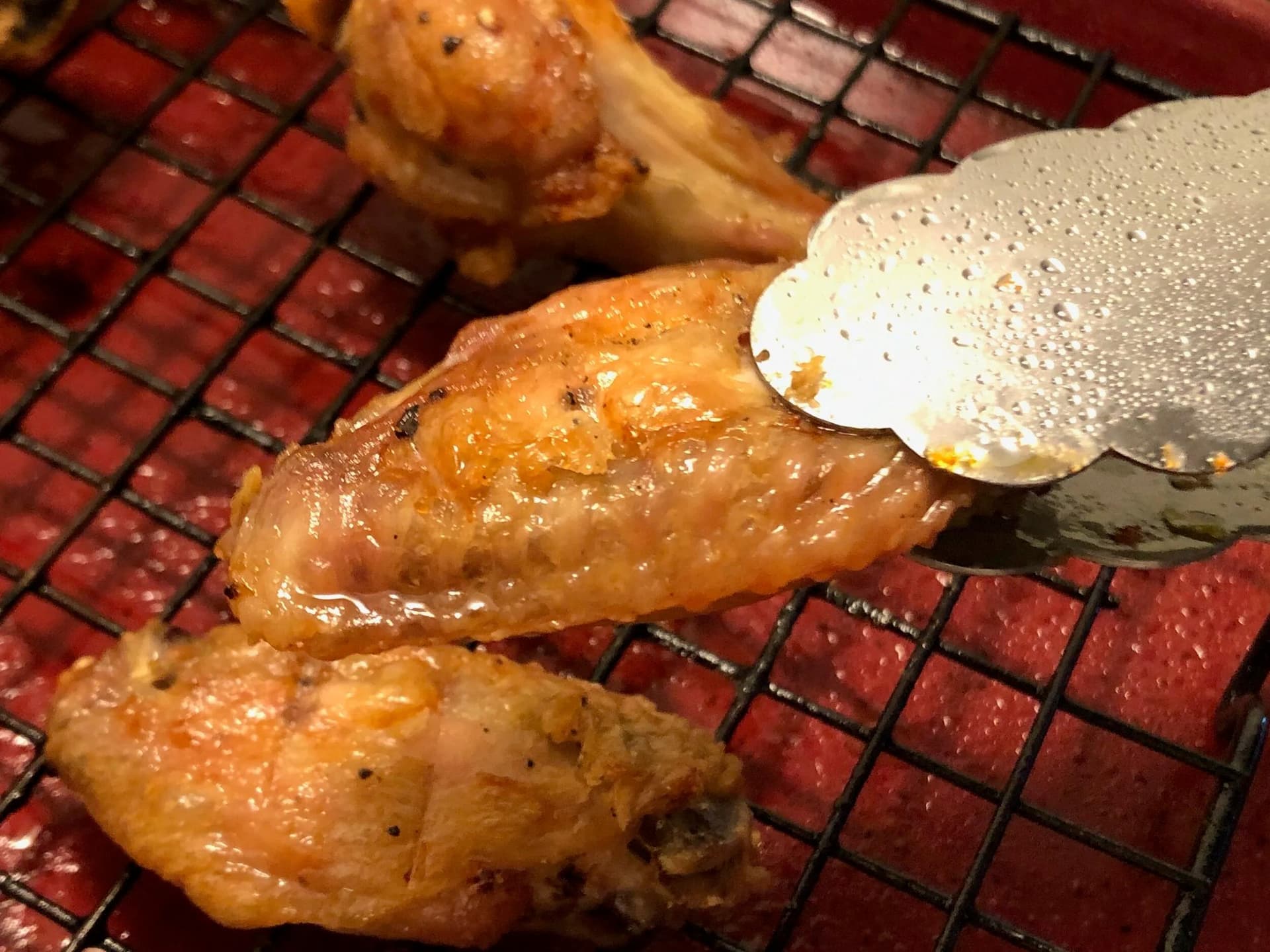 Crispy baked buffalo chicken wings on a red mesh cooling rack being brushed with sauce.