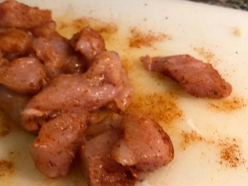 Cubed chicken pieces seasoned with Cajun spices on a light cutting board.