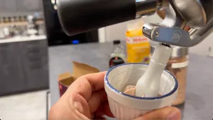 Hand holding a white bowl with blue rim while dispensing whipped cream from a whipped cream dispenser.