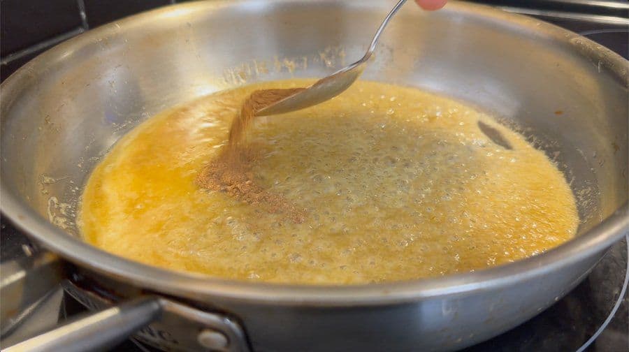 Caramel sauce simmering in a stainless steel pan with a spatula lifting the golden mixture.