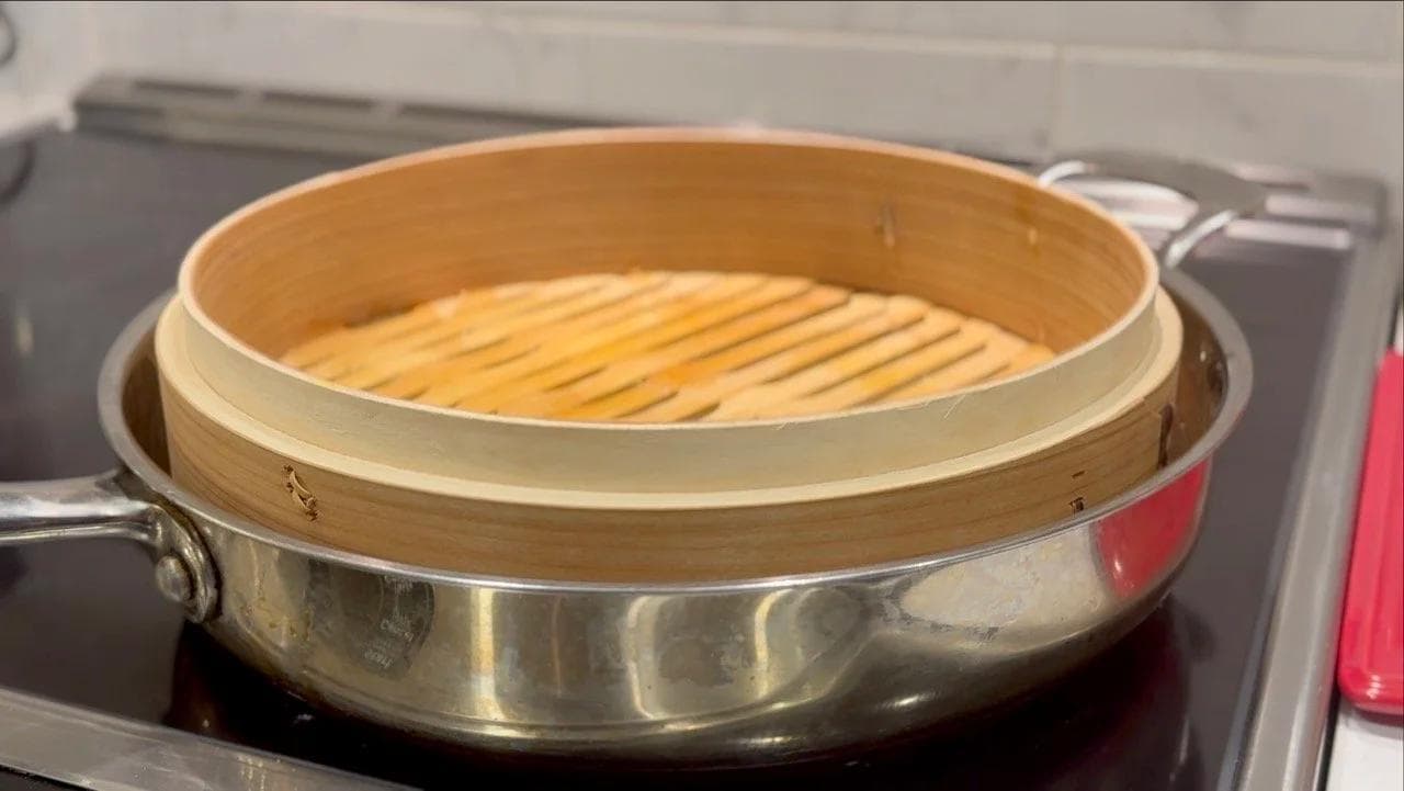 Bamboo steamer basket filled with arranged momo dumplings covered with lid, placed over boiling water in a metal pan.