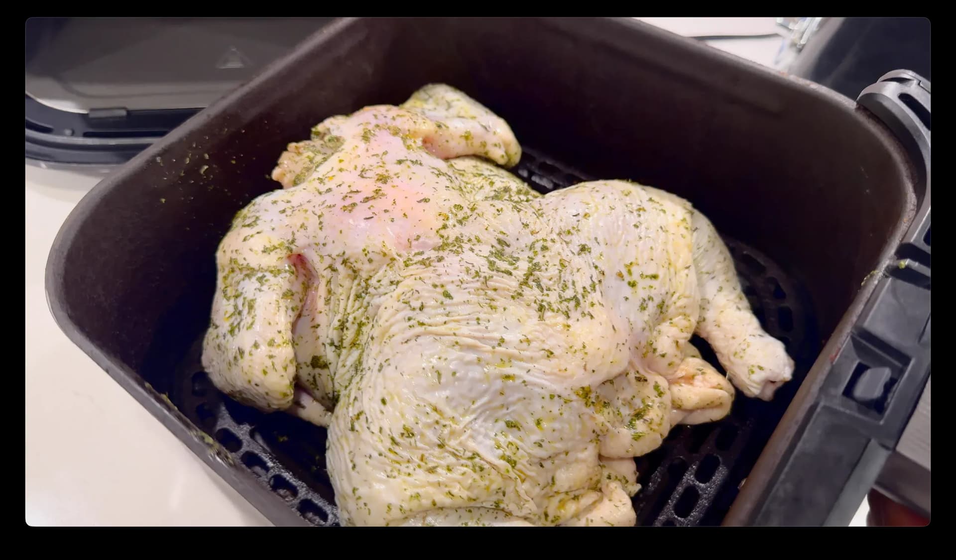 Whole chicken seasoned with herbs placed breast-side down in air fryer basket before cooking.