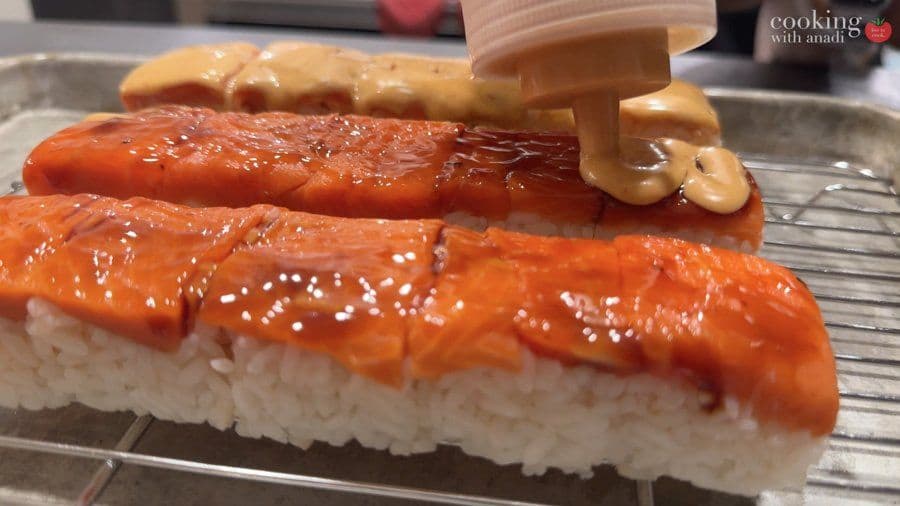 Torching oshizushi pieces with salmon topping, showing caramelized glaze and light charring on the fish.