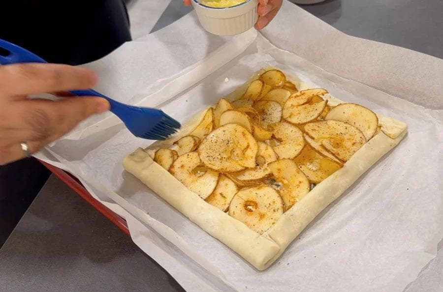 Puff pastry tart with sliced potatoes and ricotta filling, brushed with garlic butter, ready for baking.