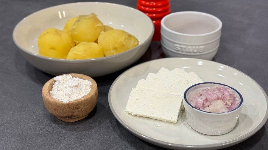 Ingredients for llapingachos: boiled Yukon gold potatoes, flour, queso cotija cheese, and diced onions on white plates.
