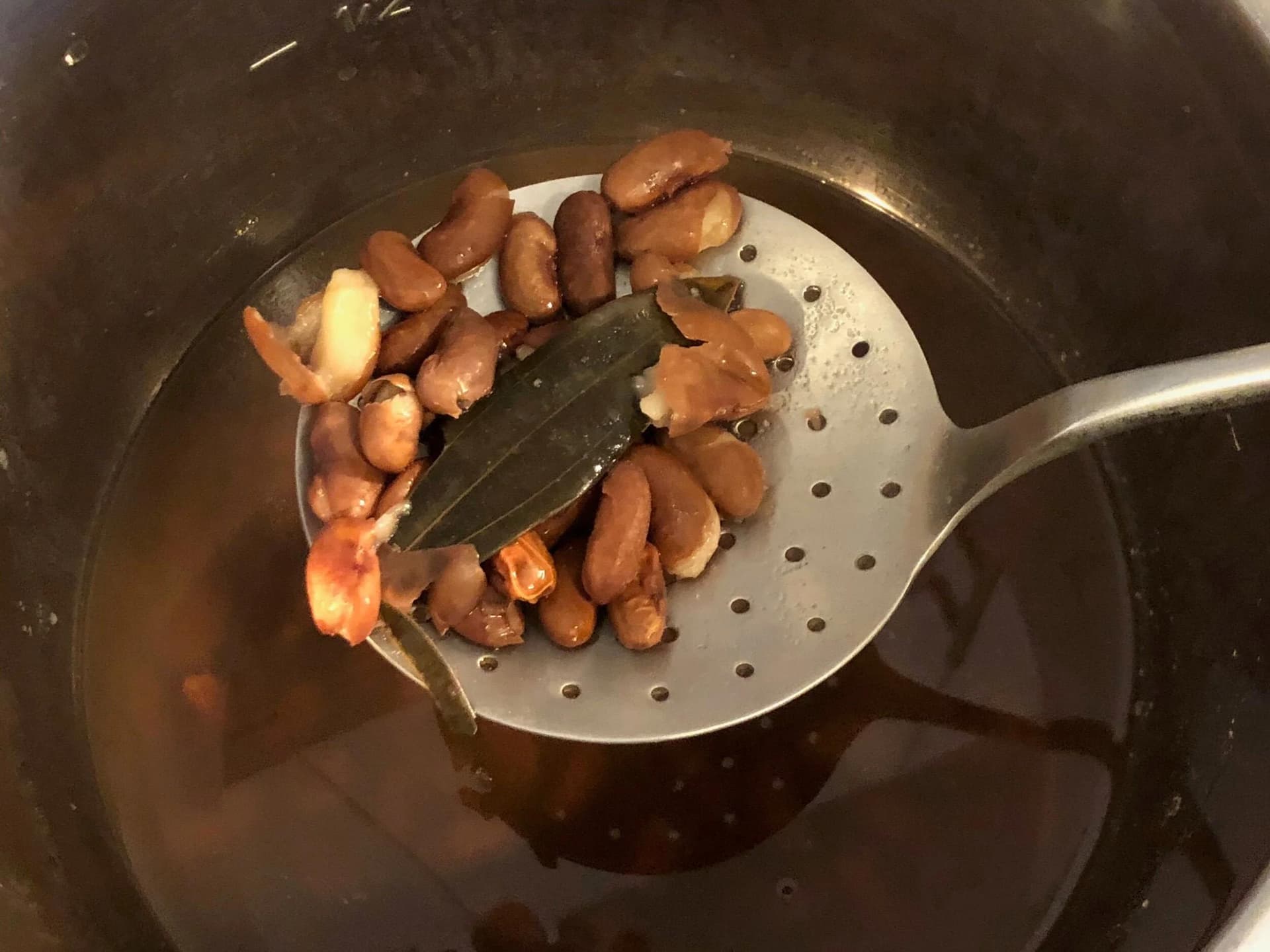 Cooked pinto beans being strained in a slotted spoon over a pot of cooking liquid.