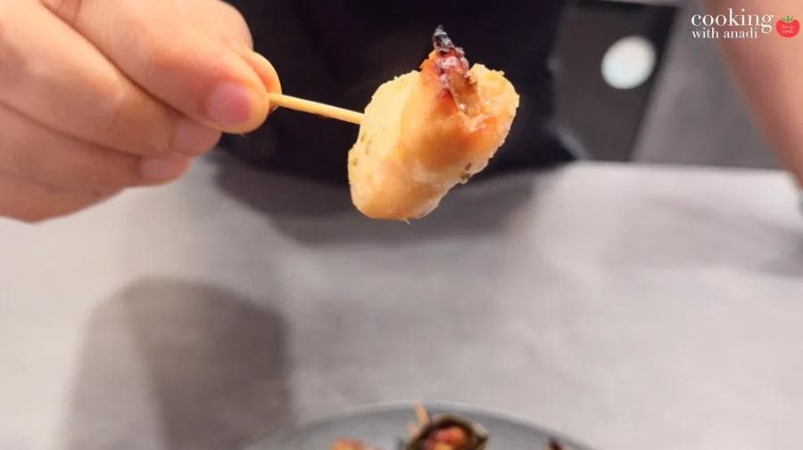 Golden-brown air fryer pandan chicken piece held on a skewer, unwrapped and ready to eat.