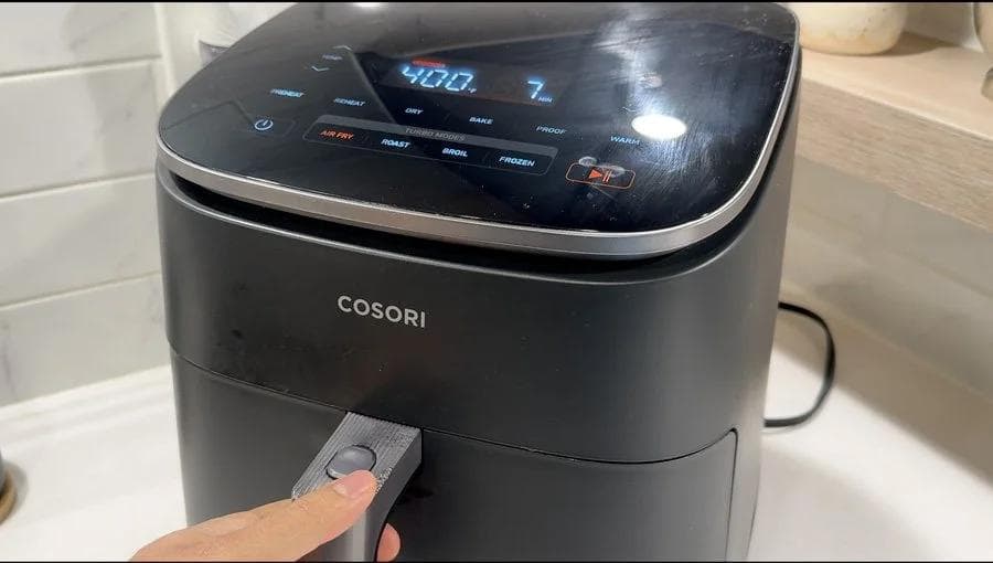 Hand pressing the air fryer button to set cooking time on a black COSORI air fryer displaying 15:00.