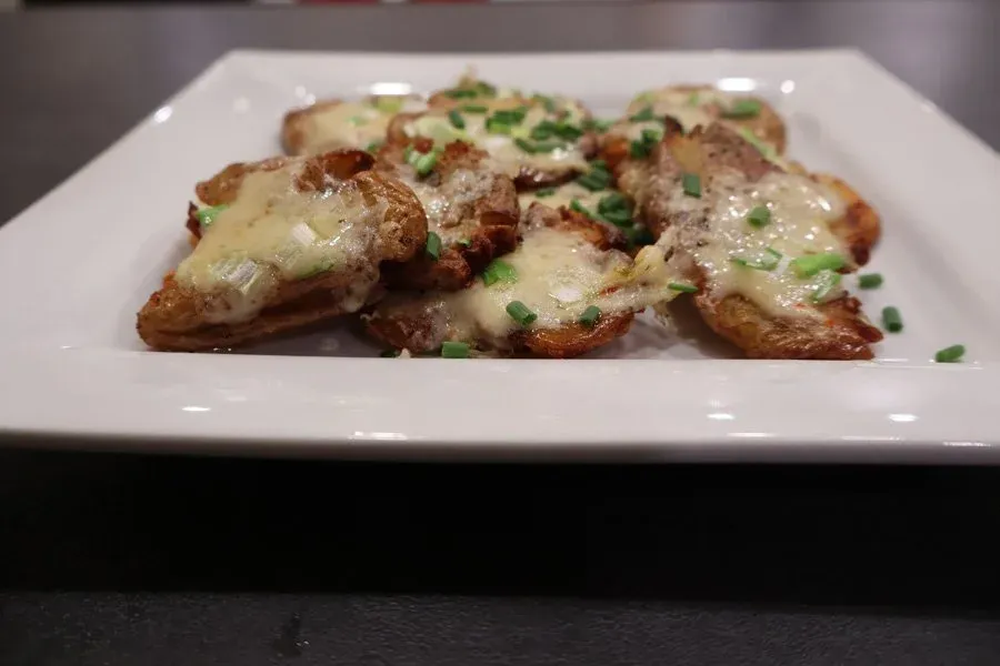 Crispy air-fried smashed potatoes topped with melted cheese and fresh chives on a white plate.