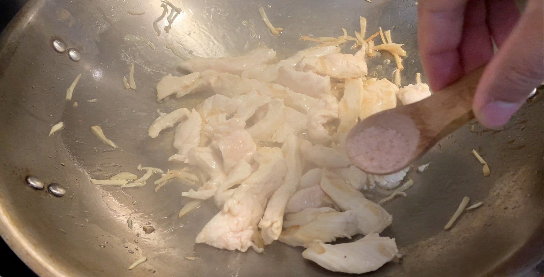 Sliced chicken being seared in a wok with garlic and sesame oil until lightly golden brown.