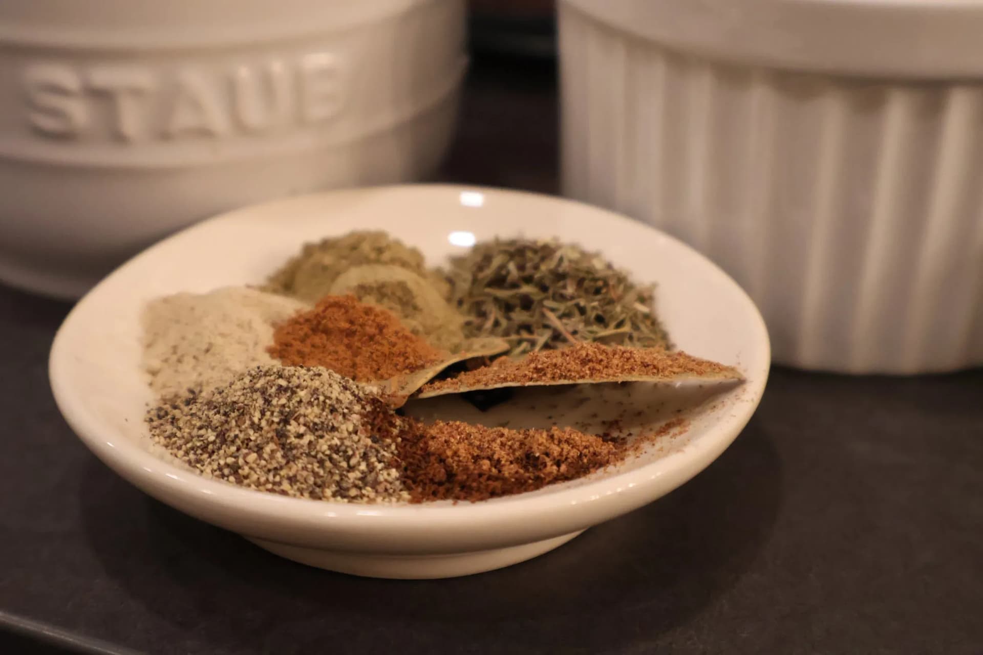 Spice blend for tourtière displayed in a white bowl showing ground cinnamon, cloves, nutmeg, and bay leaf.