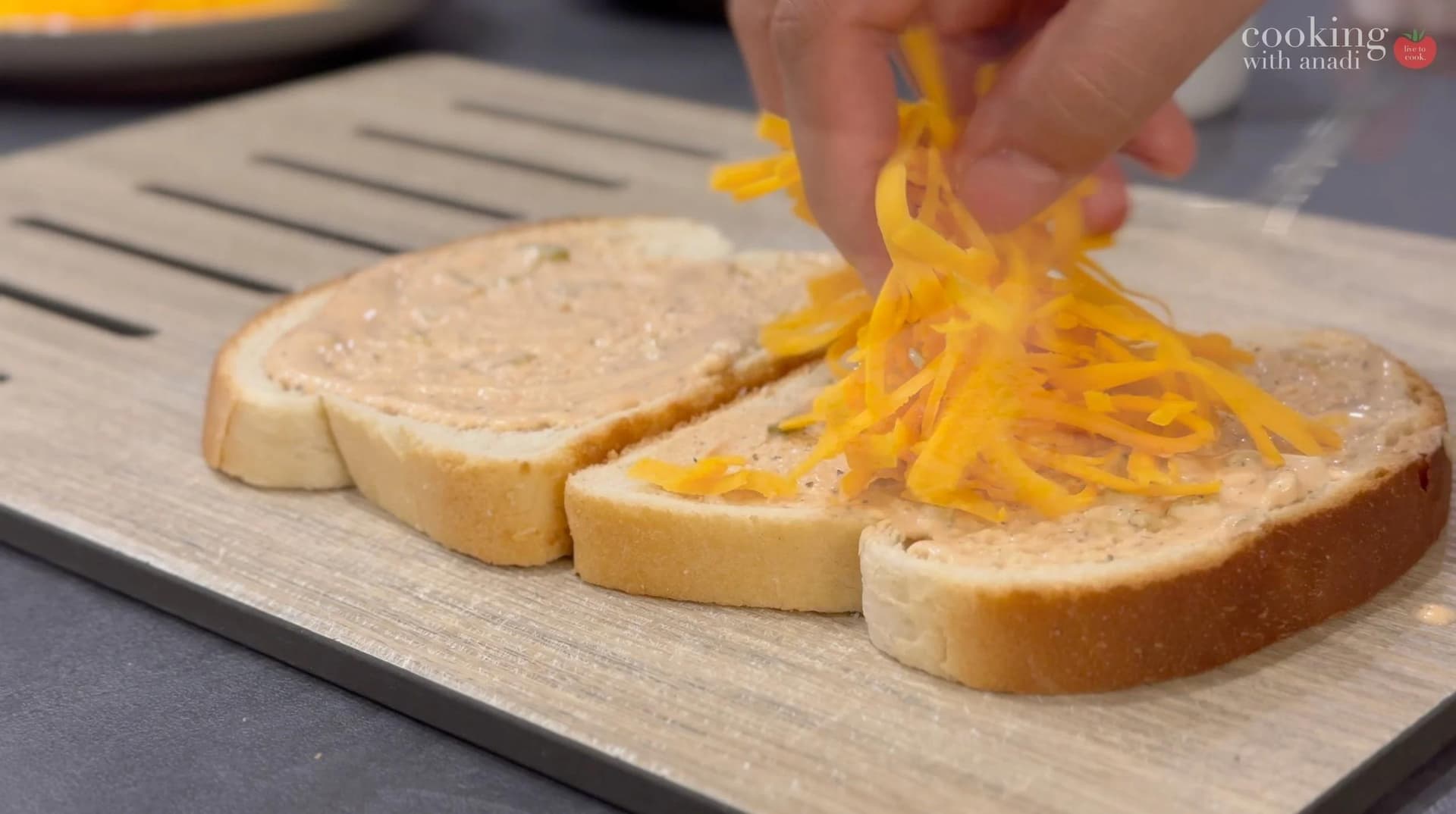 Shredded cheddar cheese being placed on sliced bread for patty melt assembly.
