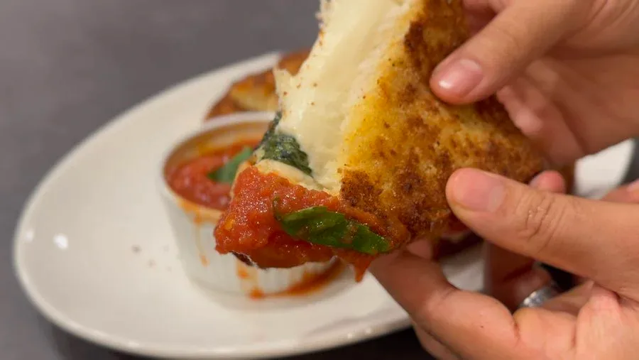 Mozzarella in Carrozza being pulled apart to show melted cheese stretching from the crispy, golden-brown fried bread sandwich with tomato and basil.