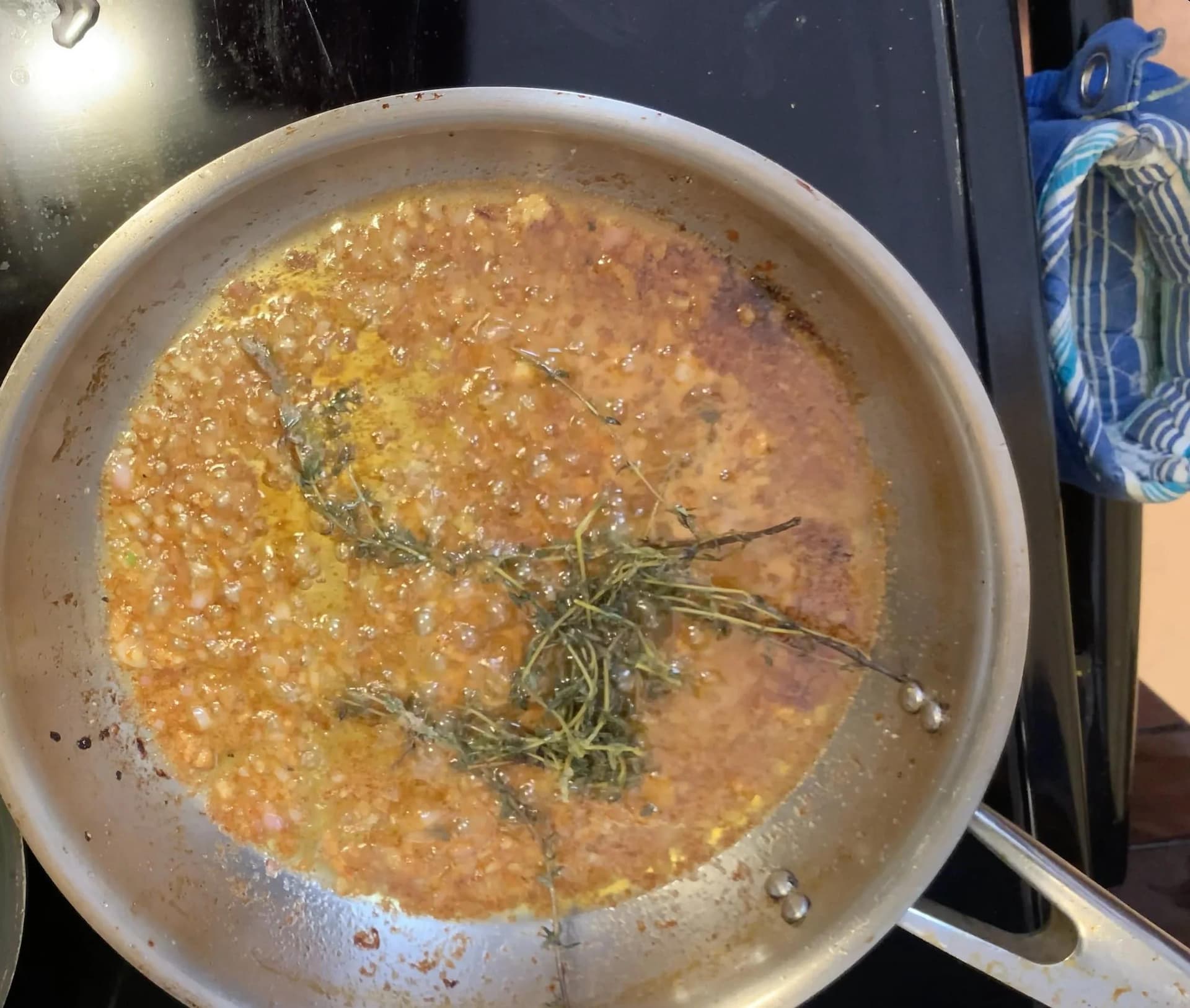 Pan of golden brown gravy with fresh thyme sprigs simmering in reduced wine and pan drippings.