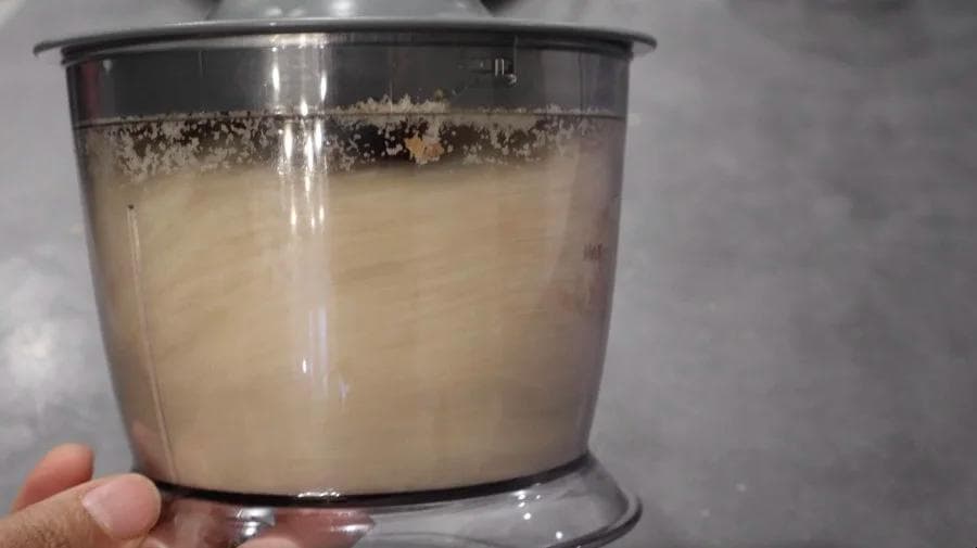 Wet batter in a food processor bowl with dark specks visible on the surface.