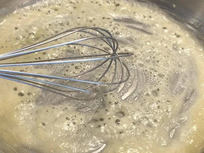Whisking butter and flour roux in a pan, showing the nutty-brown mixture before adding milk.