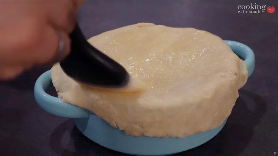 Brushing egg wash onto unbaked chicken pot pie crust in a blue dish with a pastry brush.