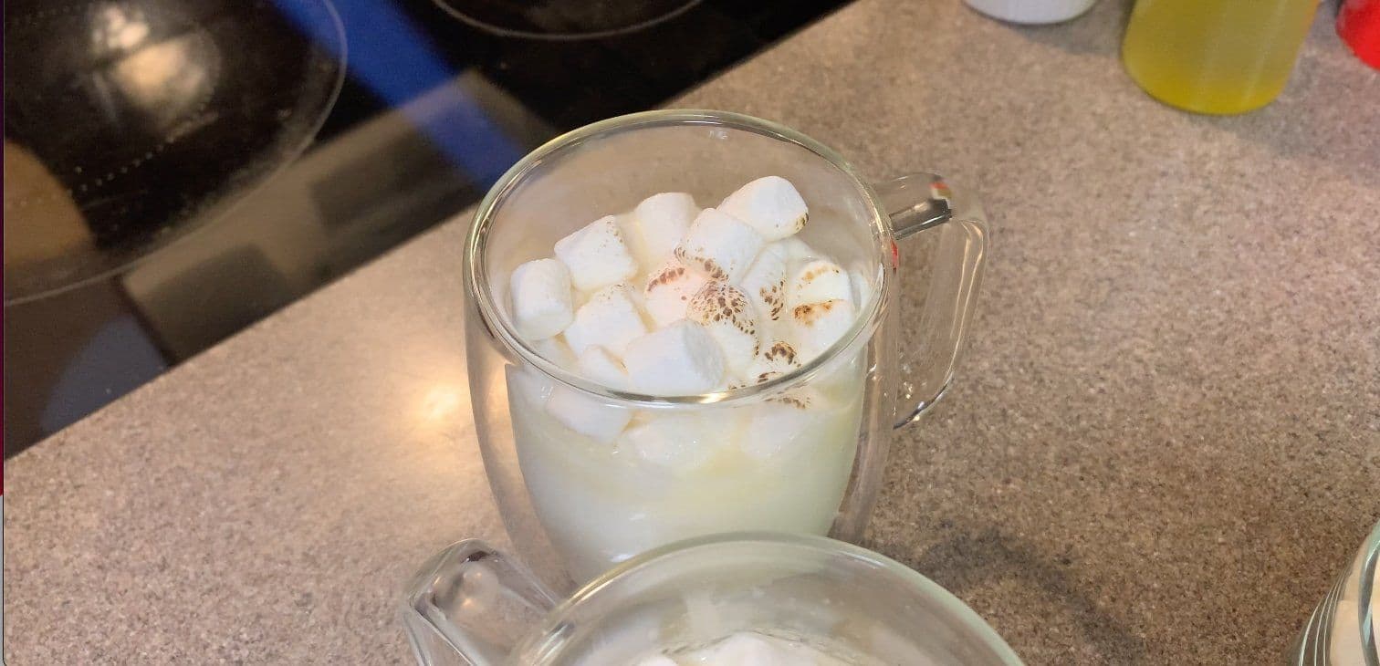 White hot chocolate topped with marshmallows and grated white chocolate in a clear mug.