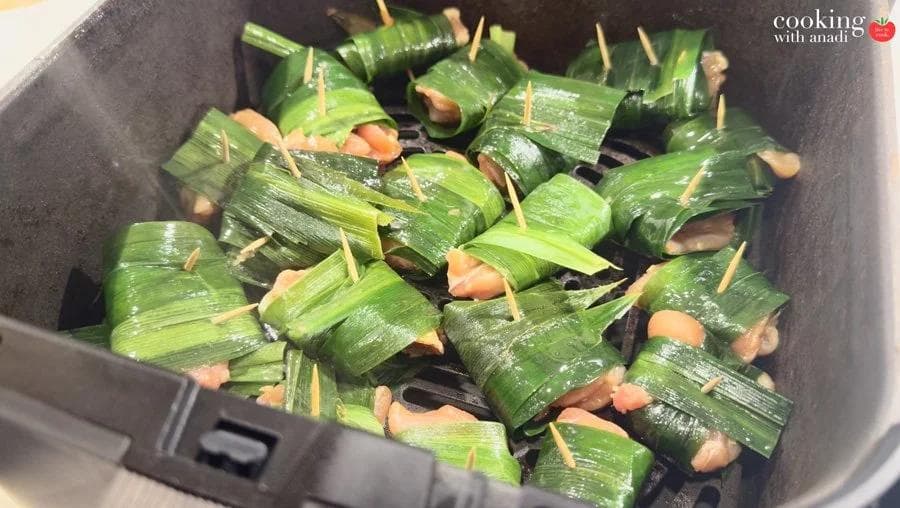 Pandan-wrapped chicken pieces secured with toothpicks arranged in a single layer in an air fryer basket, ready to cook.