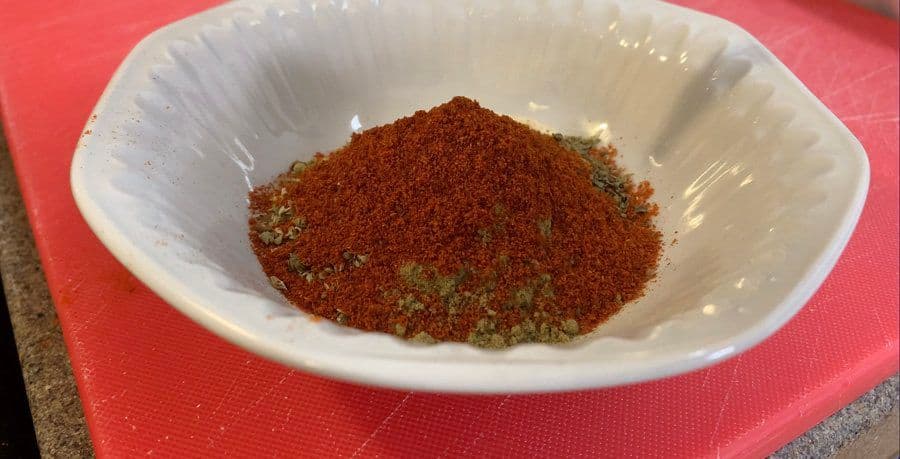 Homemade spice mix for buffalo chicken in a white bowl, combining red and green spices.